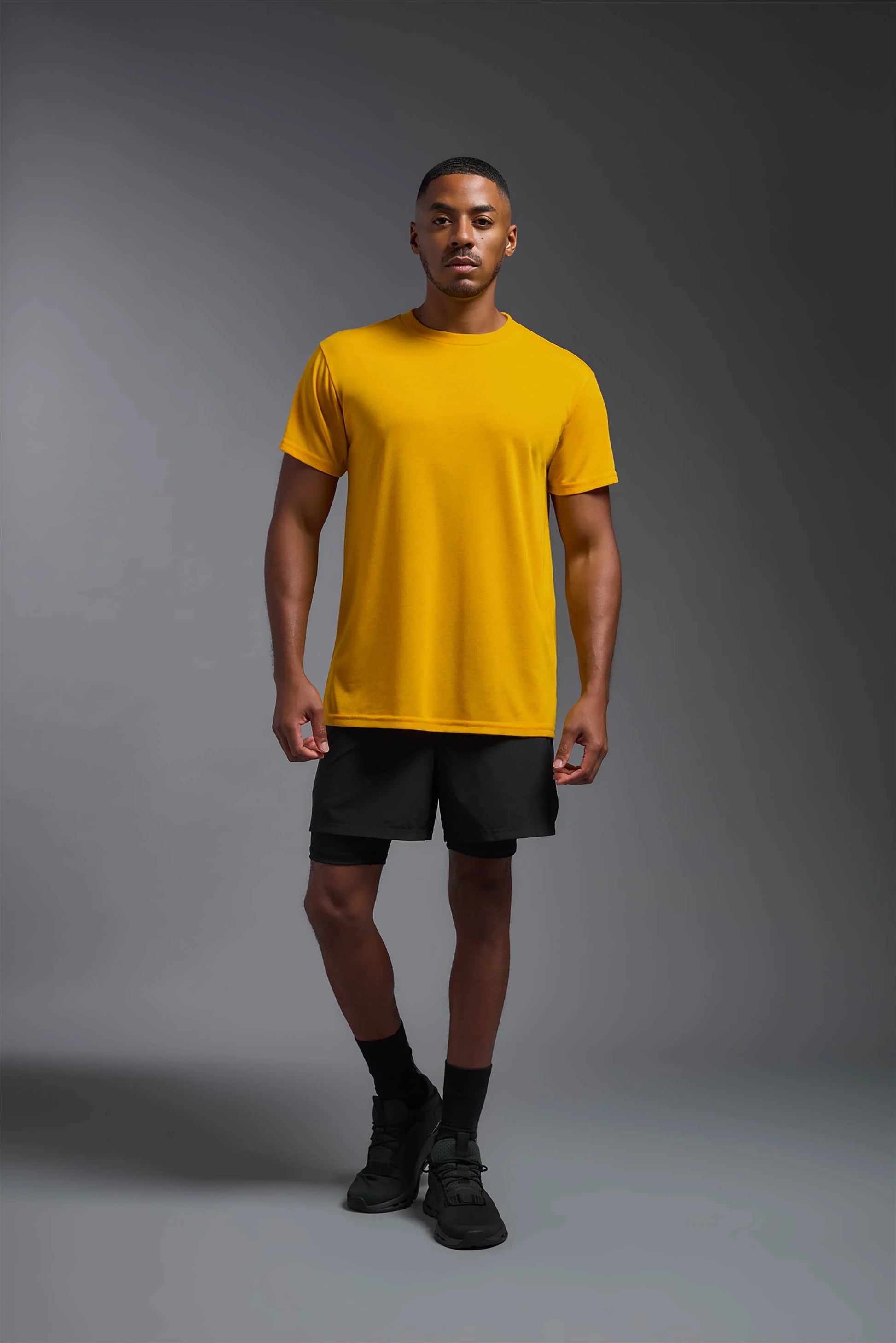 Man wearing a yellow t-shirt and black shorts on a gray background