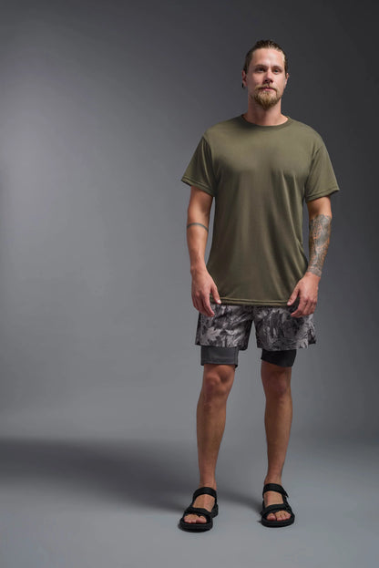 Man wearing a green t-shirt and camouflage shorts on a gray background