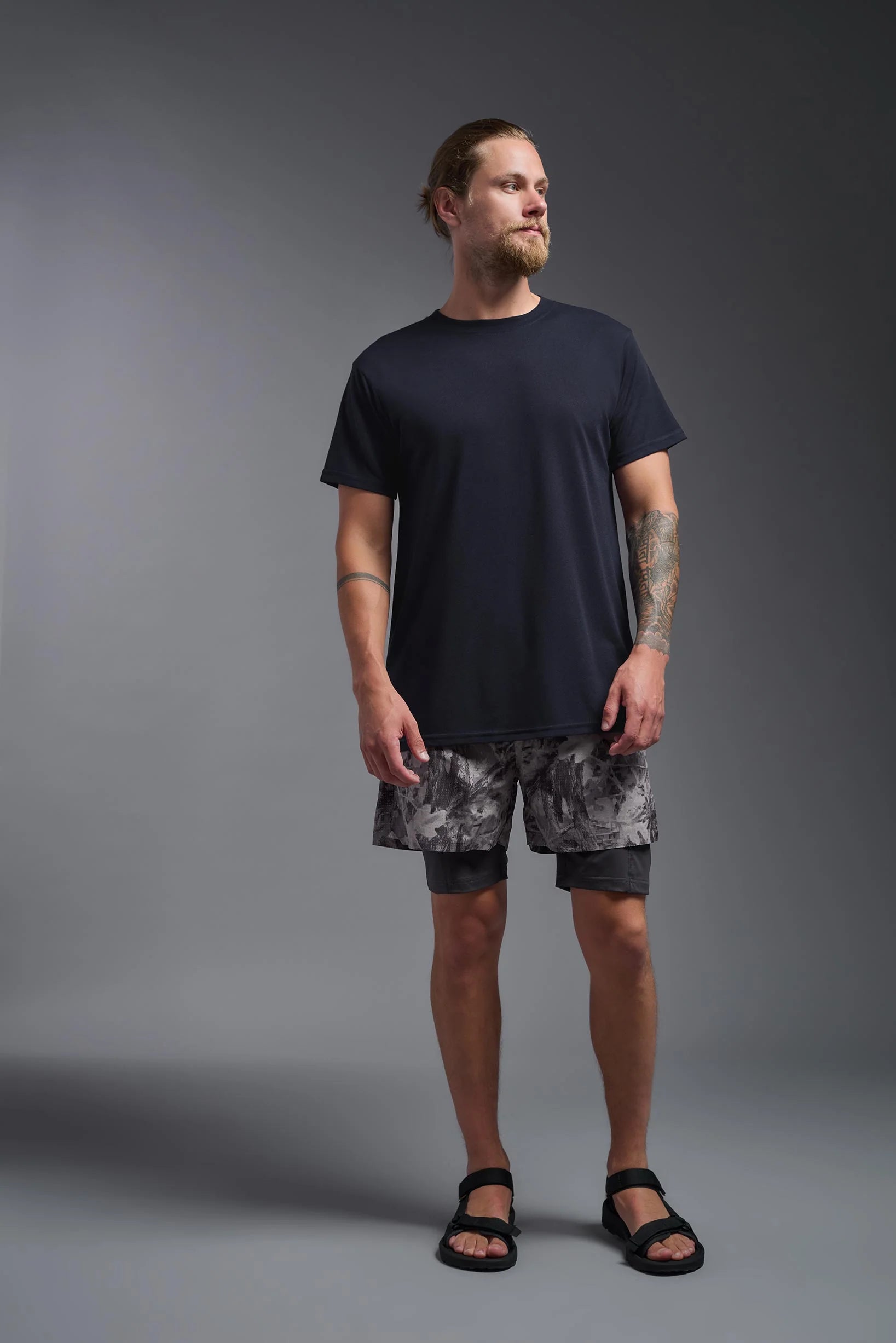 Man wearing a black t-shirt and camouflage shorts on a gray background