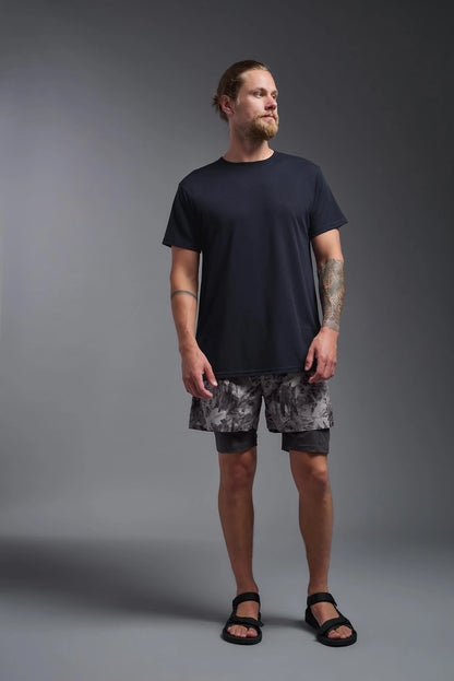 Man wearing a black t-shirt and camouflage shorts on a gray background