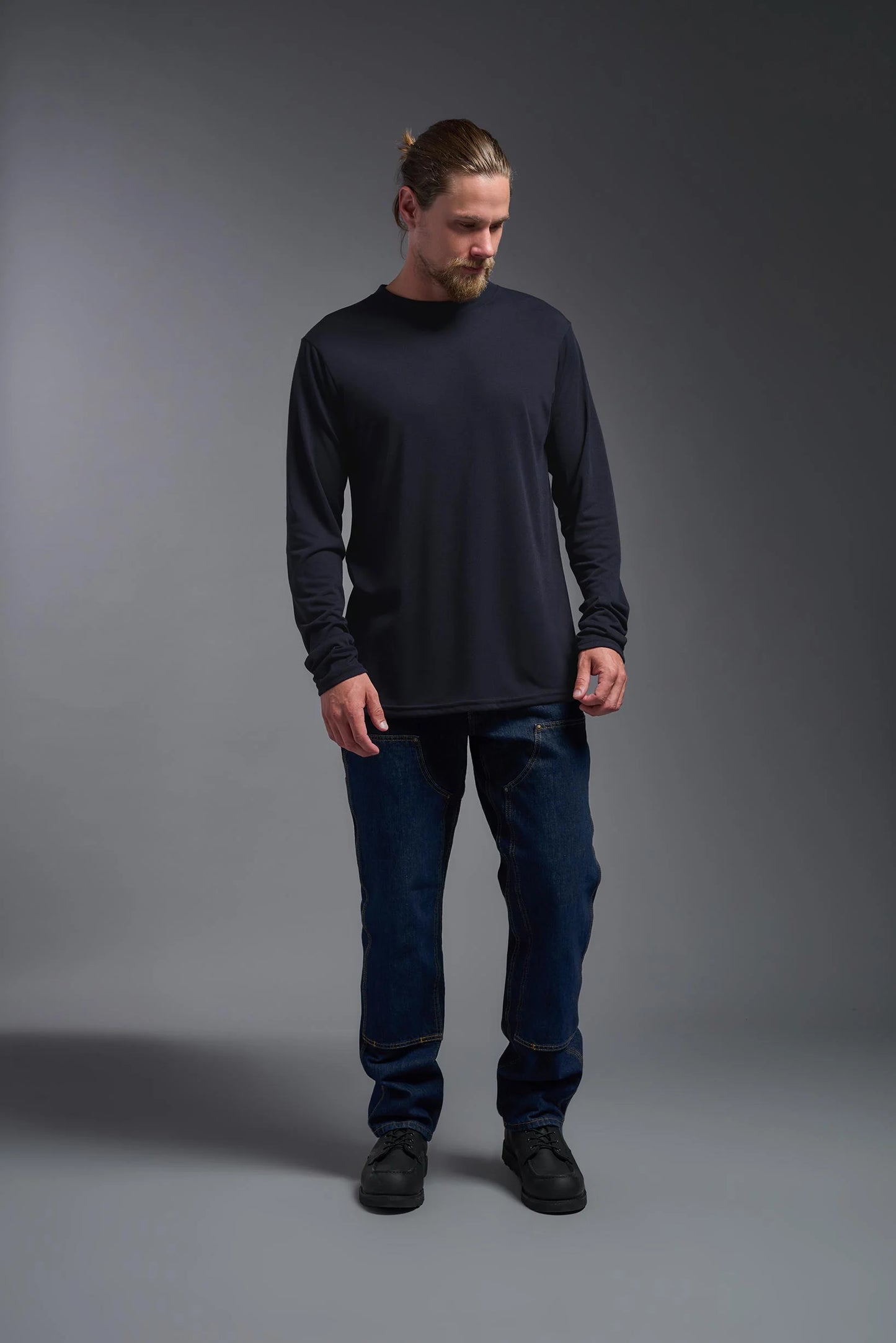 Man wearing a black long-sleeve shirt and blue jeans against a gray background