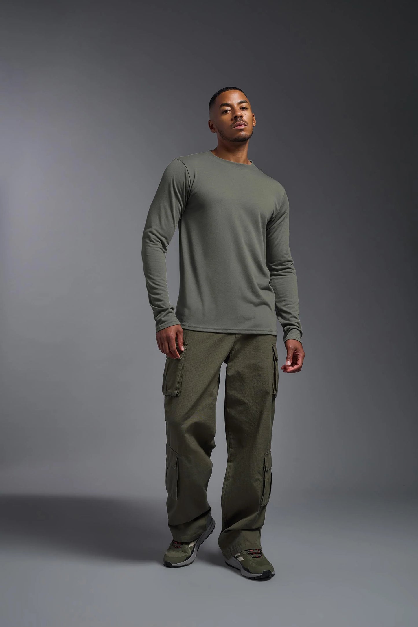 Man wearing a green long-sleeve shirt and cargo pants on a gray background