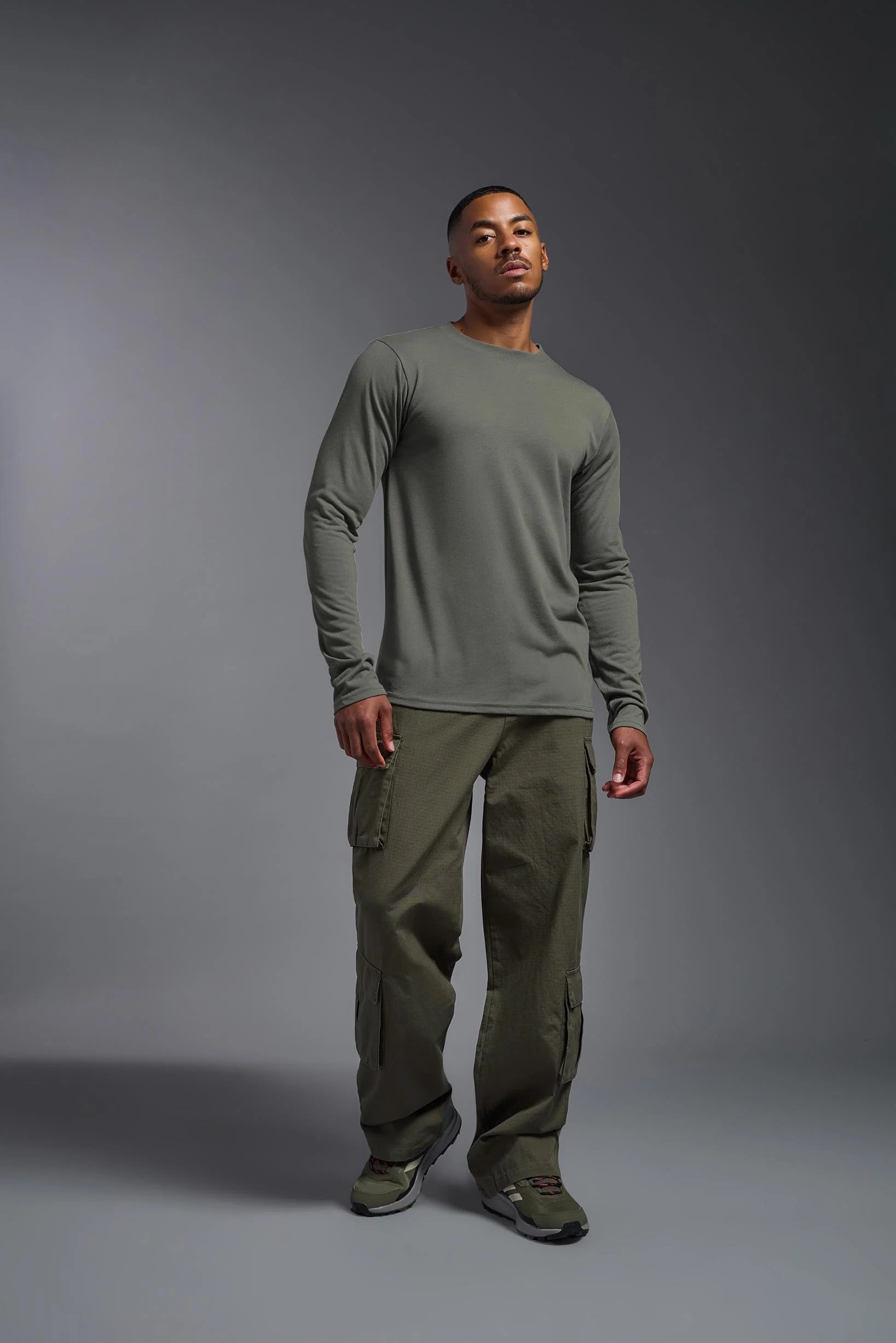 Man wearing a green long-sleeve shirt and cargo pants on a gray background