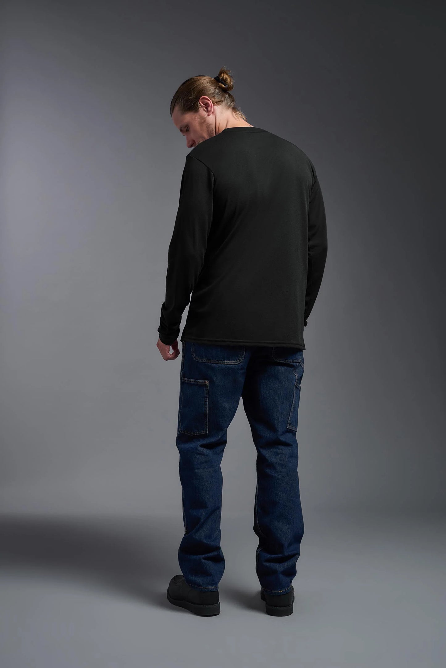 Person wearing a black long-sleeve shirt and blue jeans against a gray background