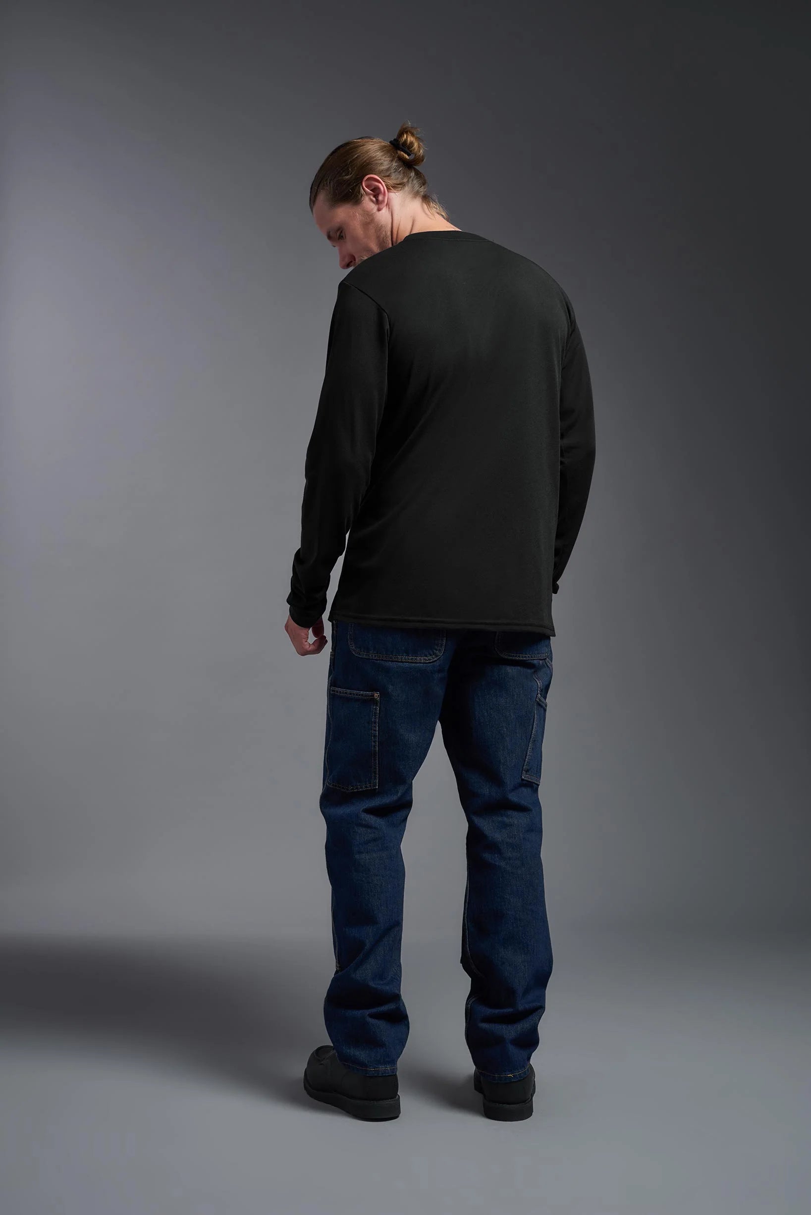 Person wearing a black long-sleeve shirt and blue jeans against a gray background