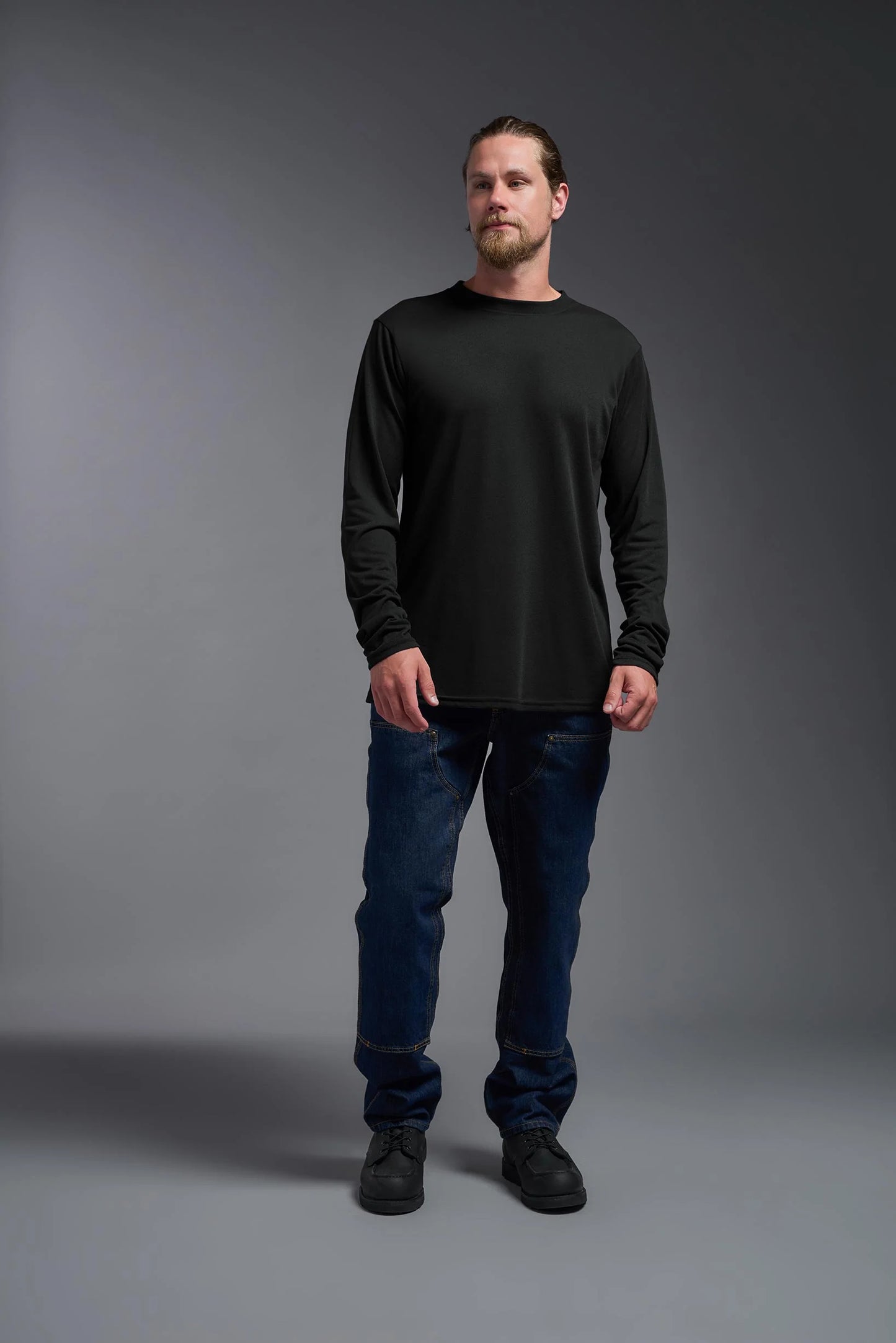 Man wearing a black long-sleeve shirt and blue jeans against a gray background