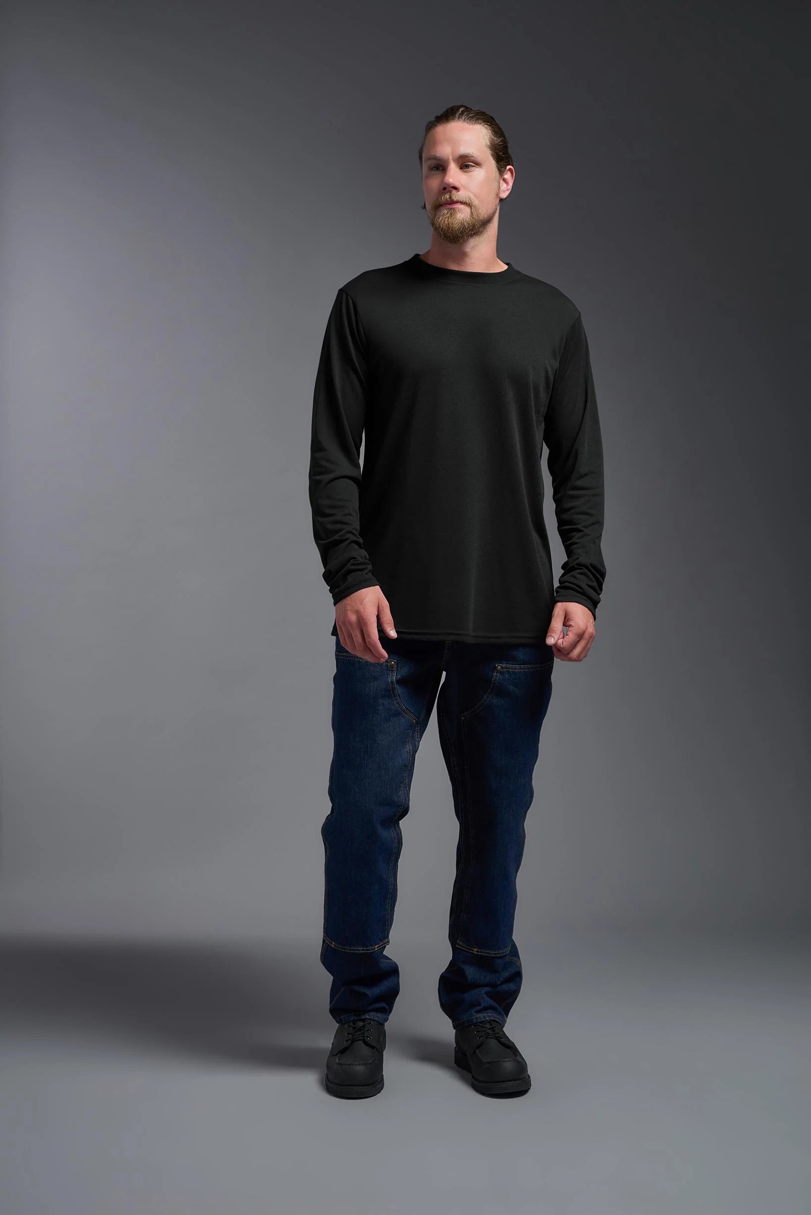 Man wearing a black long-sleeve shirt and blue jeans against a gray background