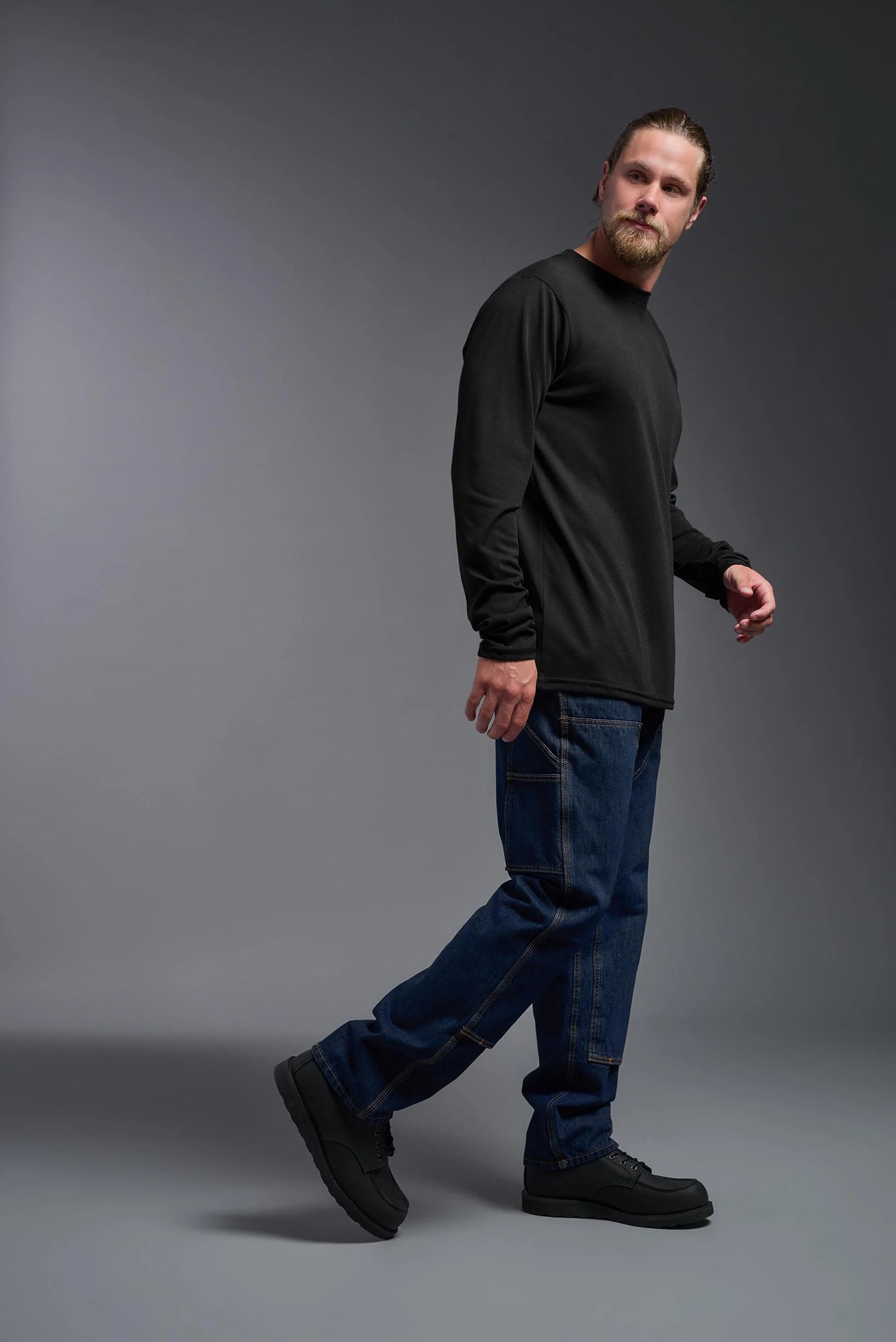 Man wearing a black long-sleeve shirt and blue jeans on a gray background