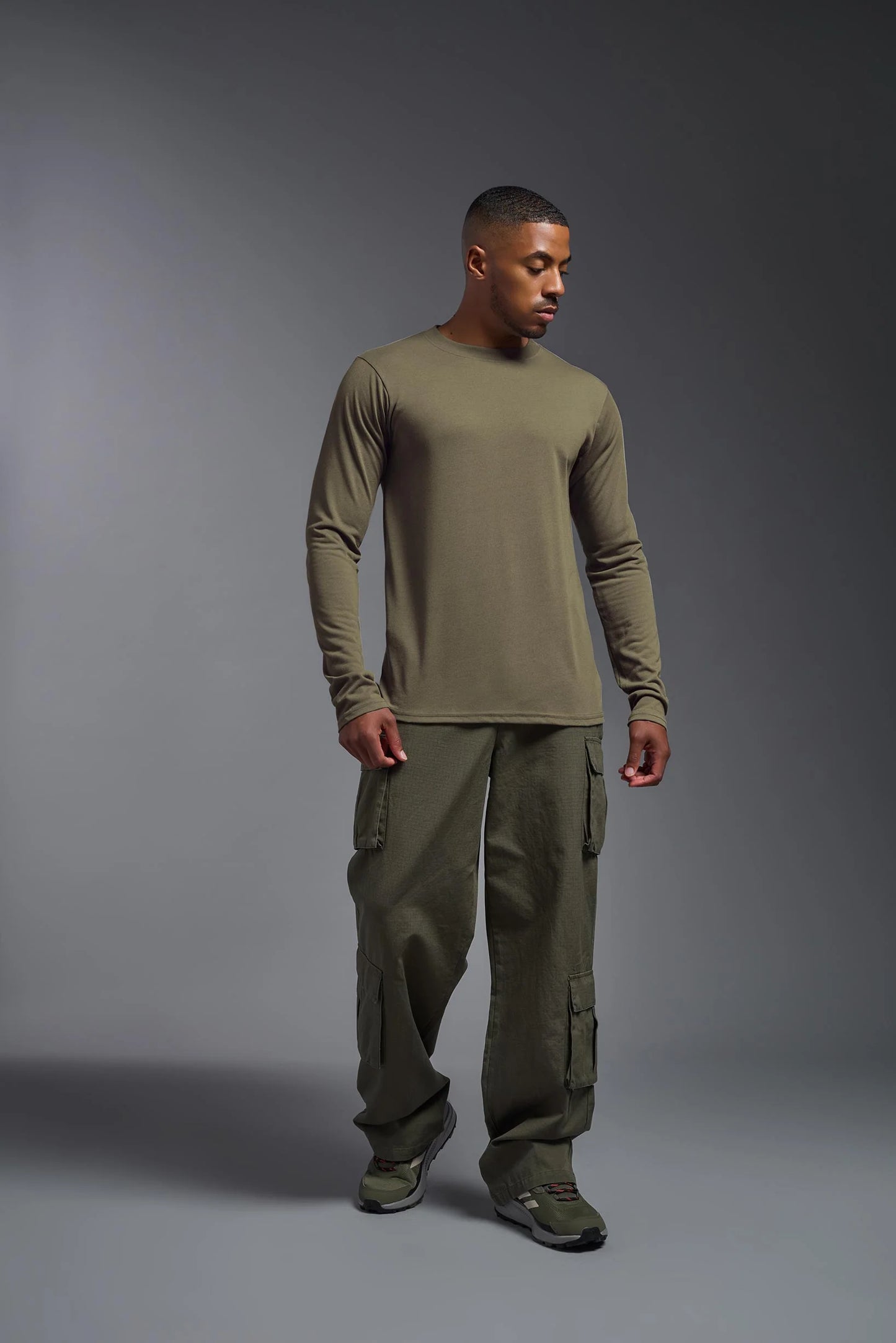 Man wearing a green long-sleeve shirt and cargo pants on a gray background