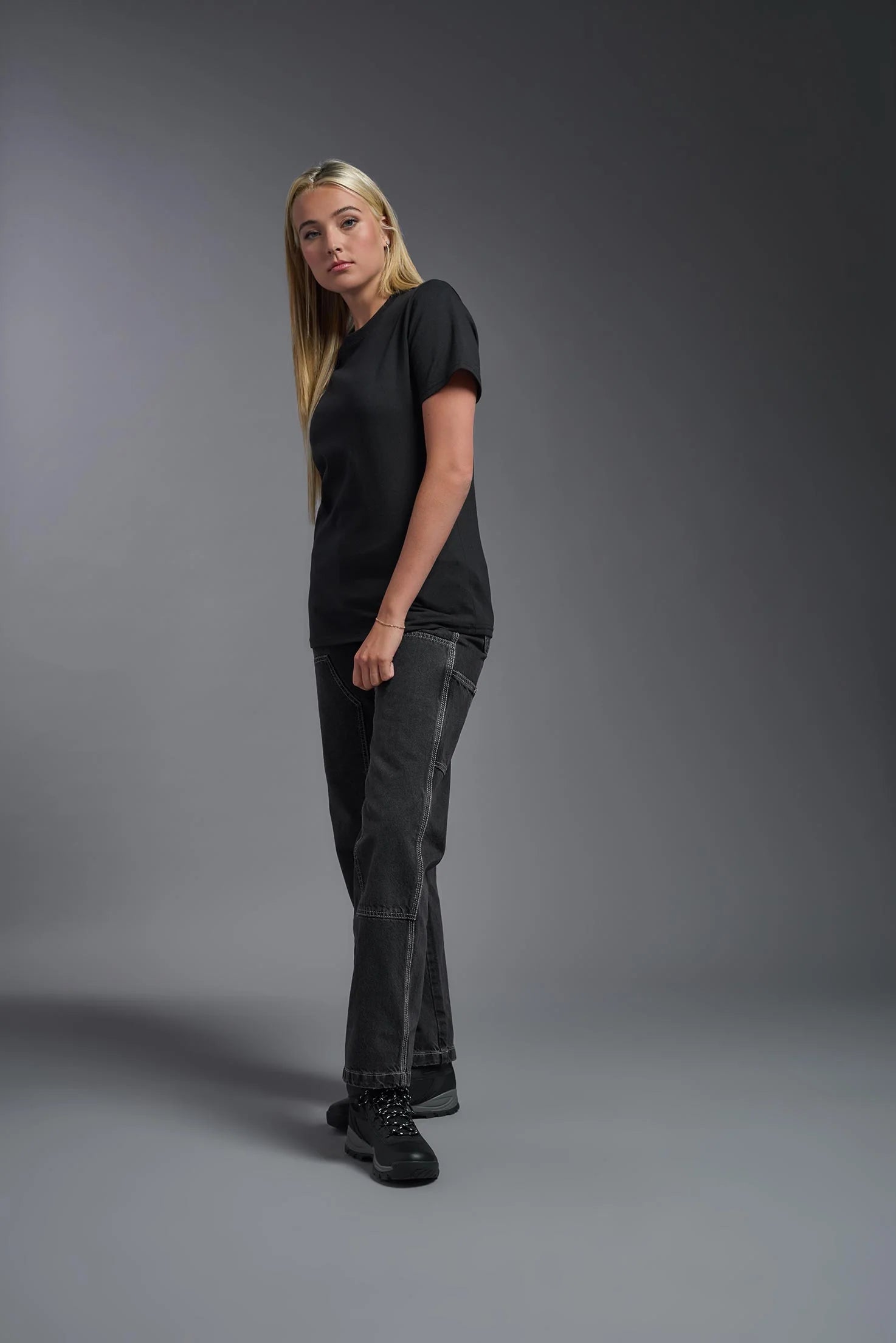 Person wearing a black t-shirt and dark jeans against a gray background