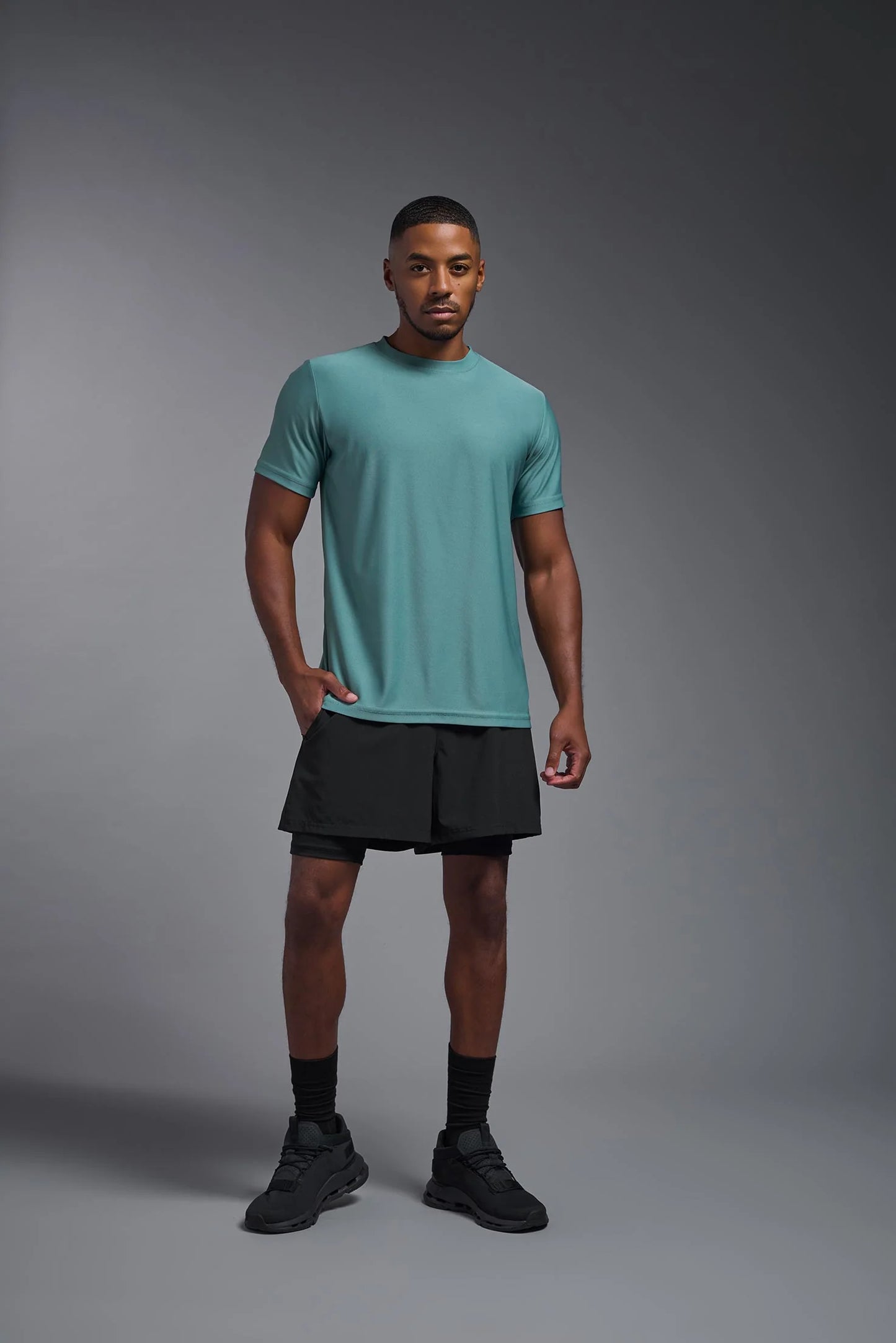 Man wearing a teal t-shirt and black shorts on a gray background