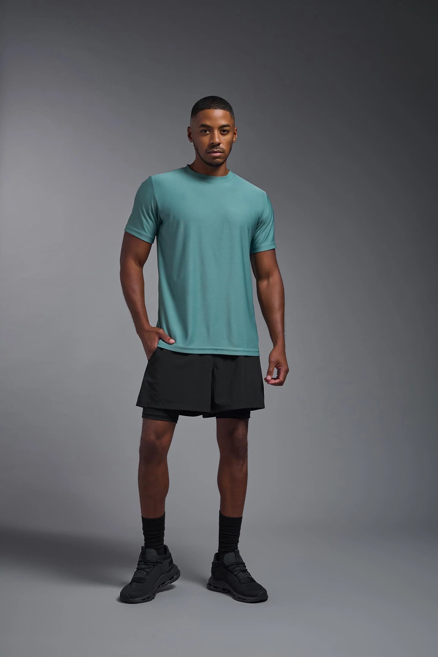 Man wearing a teal t-shirt and black shorts on a gray background