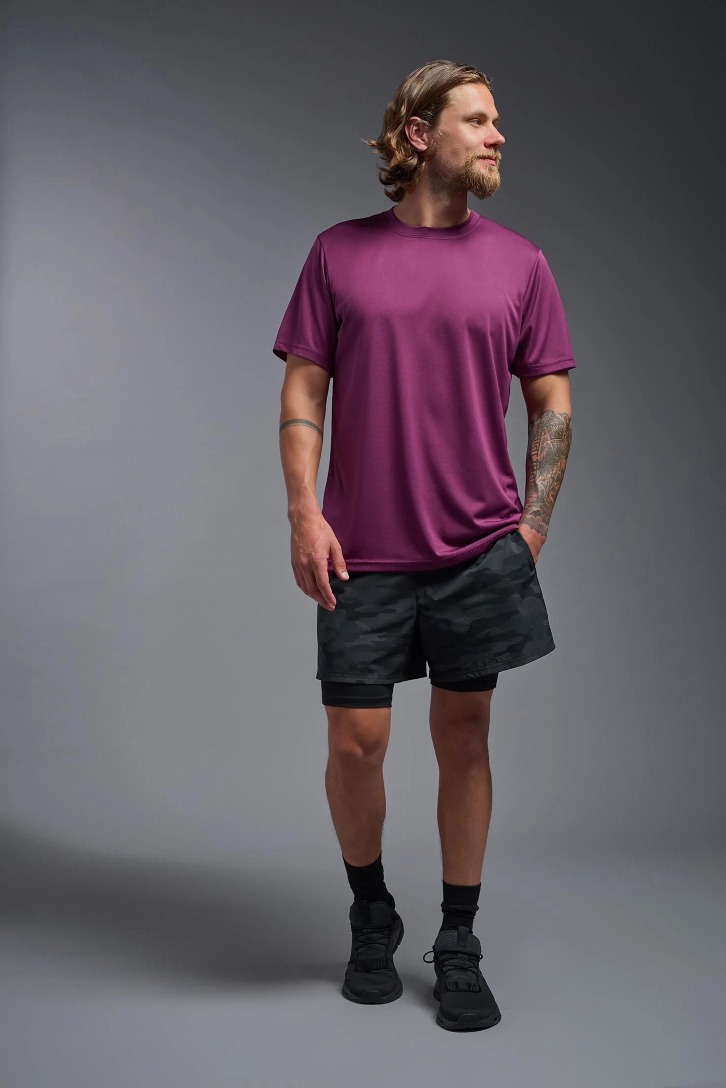 Man wearing a purple t-shirt and black shorts on a gray background