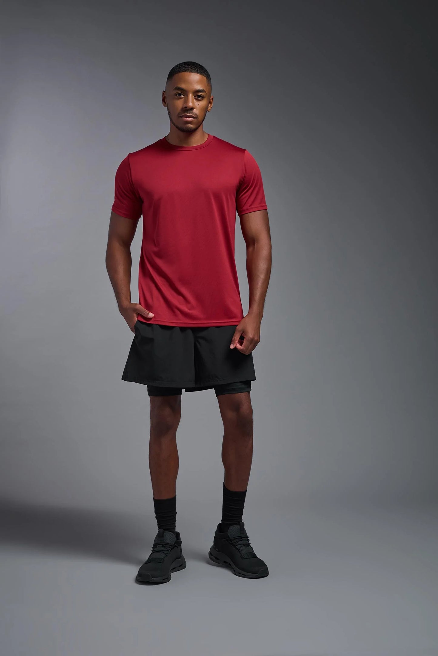 Man wearing a red athletic shirt and black shorts on a gray background