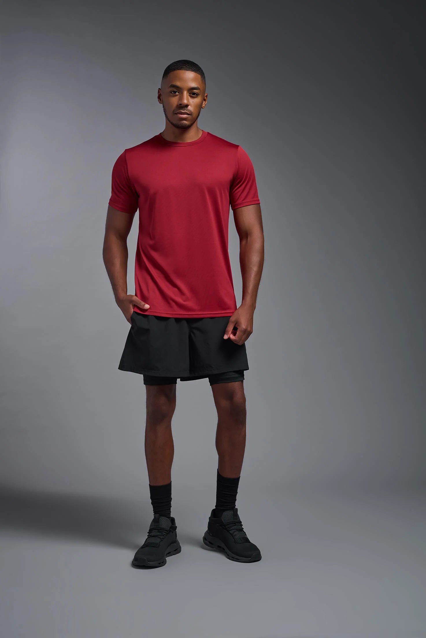 Man wearing a red athletic shirt and black shorts on a gray background