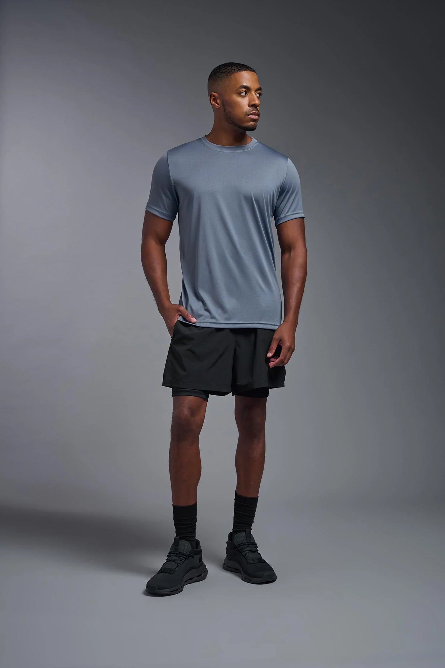 Man wearing a gray t-shirt and black shorts standing against a gray background