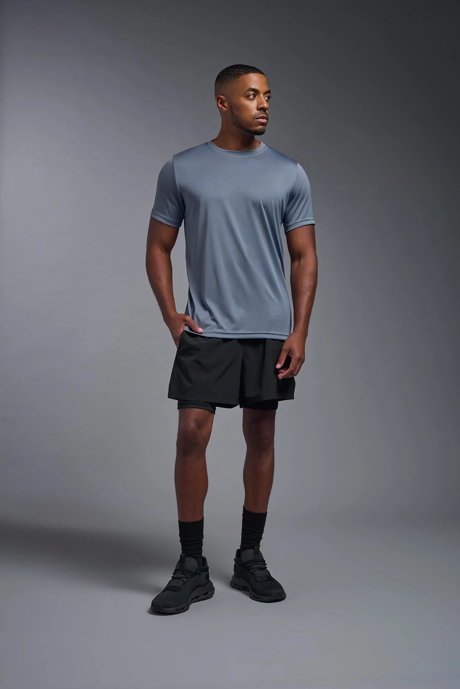 Man wearing a gray t-shirt and black shorts standing against a gray background