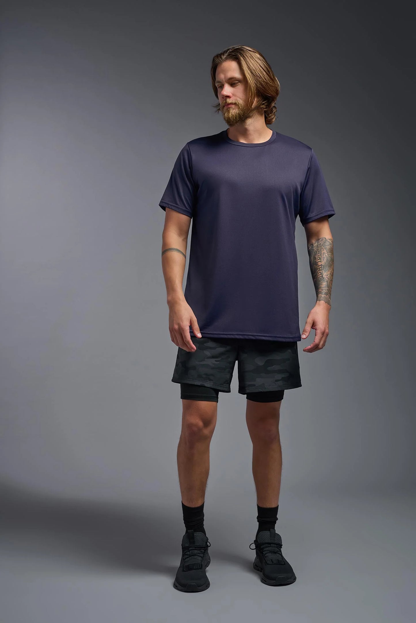 Man wearing a dark purple t-shirt and black shorts on a gray background