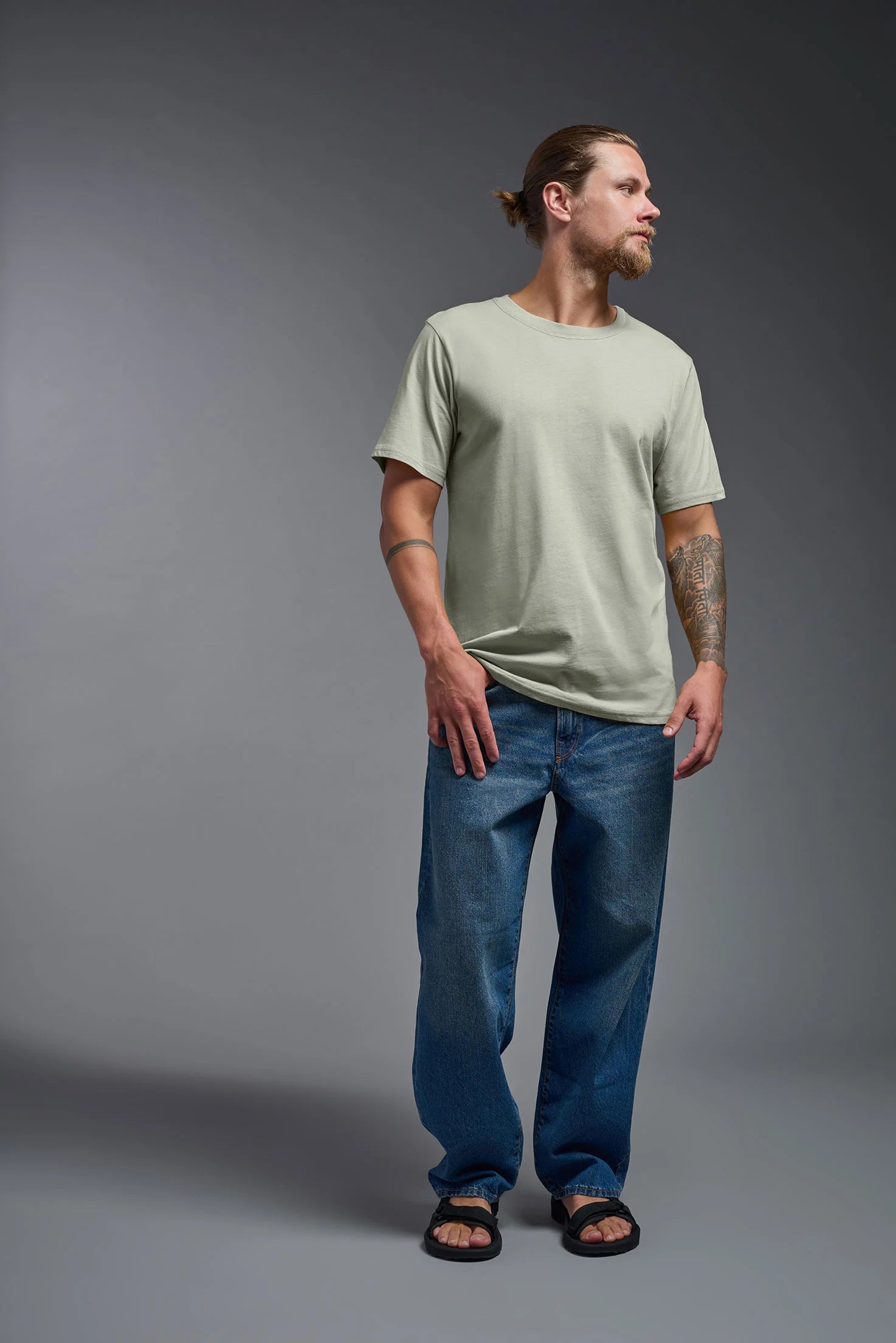 Man wearing a light green t-shirt and blue jeans against a gray background