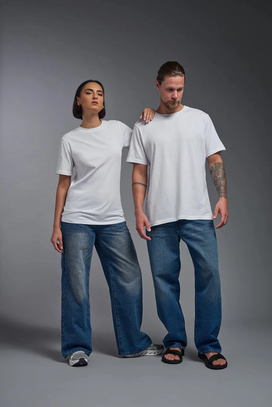 Two people wearing white t-shirts and blue jeans standing against a gray background