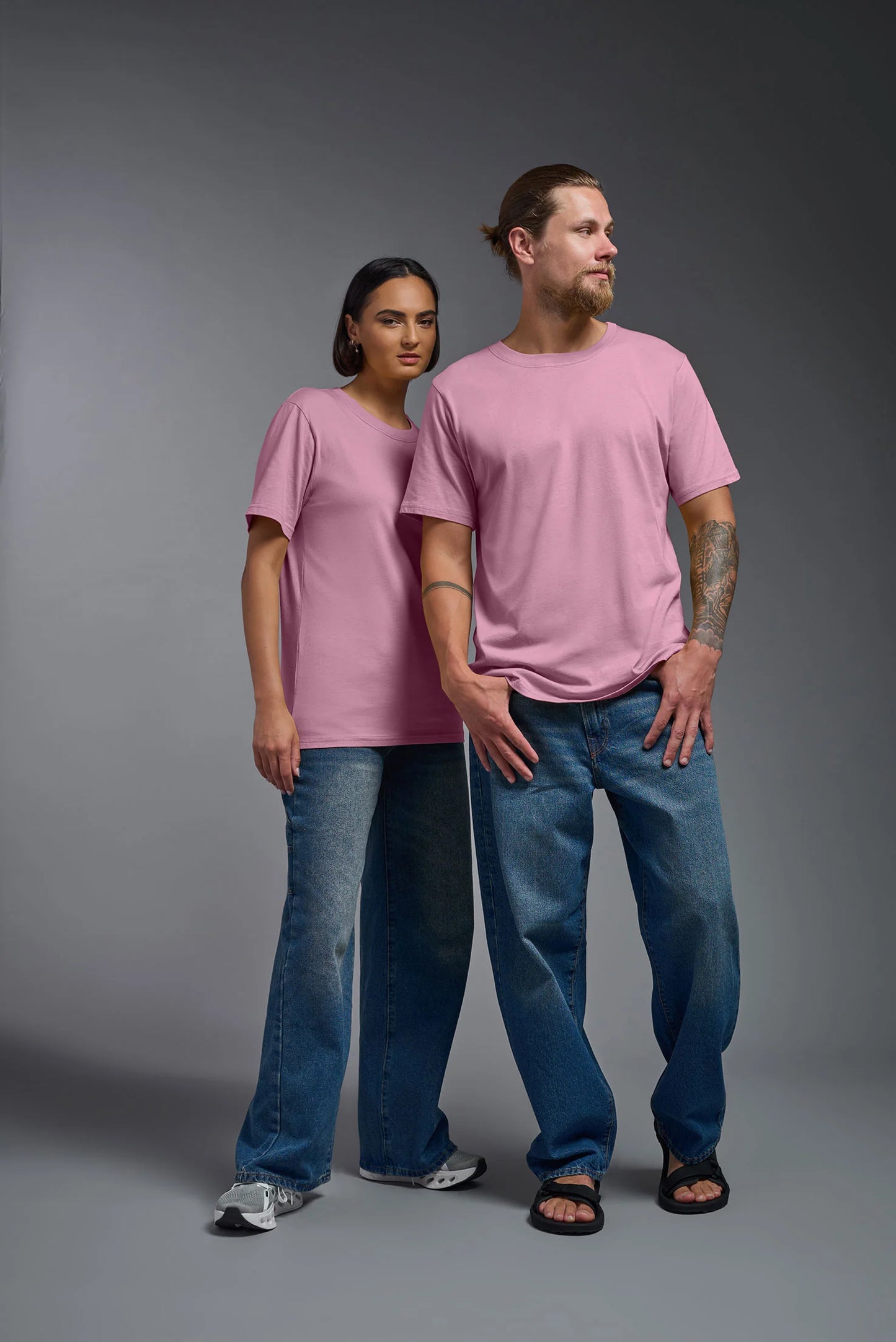 Two people wearing matching pink t-shirts and blue jeans on a gray background