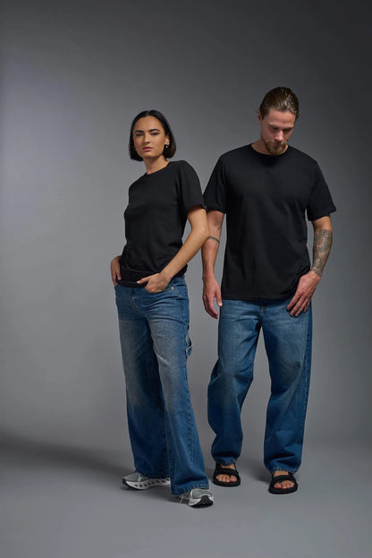 Two people wearing black t-shirts and blue jeans standing against a gray background