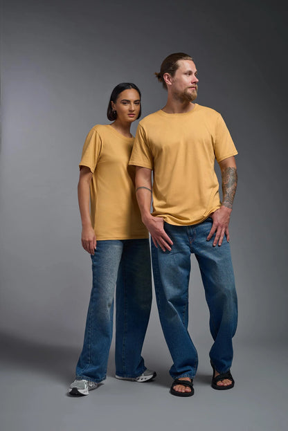 Two people wearing matching mustard yellow t-shirts and blue jeans on a gray background