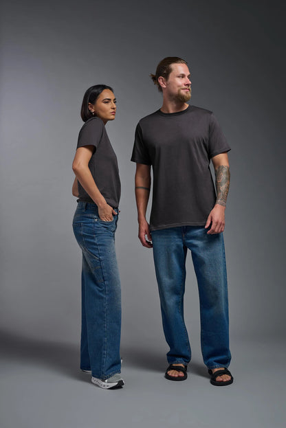 Two people wearing black t-shirts and blue jeans standing against a gray background