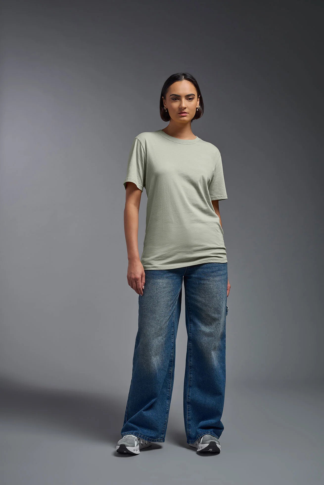 Person wearing a light green t-shirt and blue jeans on a gray background