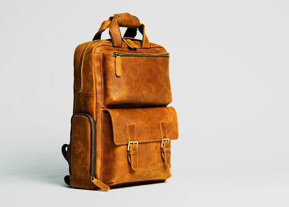 Brown leather camera backpack with front pocket, buckled straps, and top handle