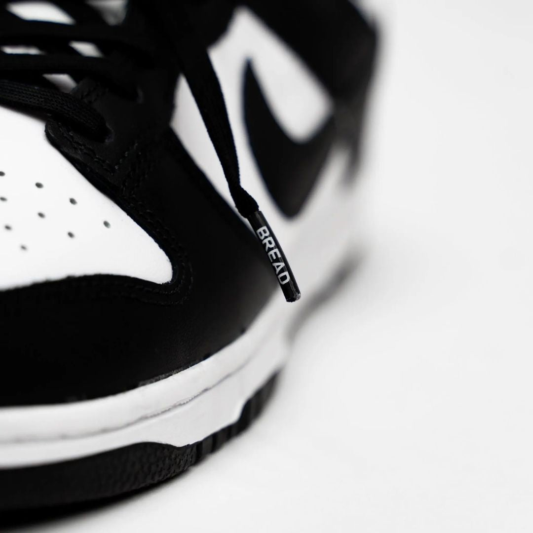 Close-up of a black and white sneaker with 'Bread' branding on the lace.