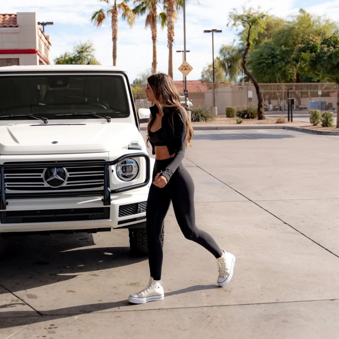 Woman in black athletic wear standing next to a white Mercedes-Benz G-Class SUV.