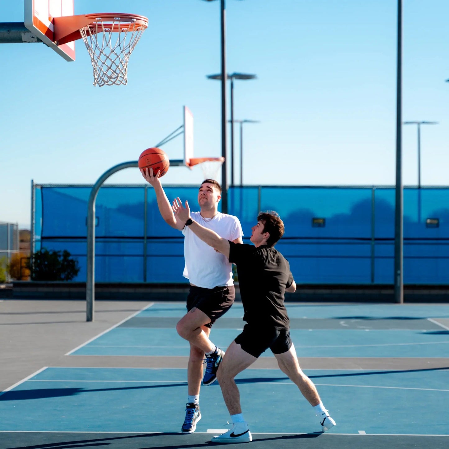 Two men playing basketball on an outdoor court with a clear blue sky.