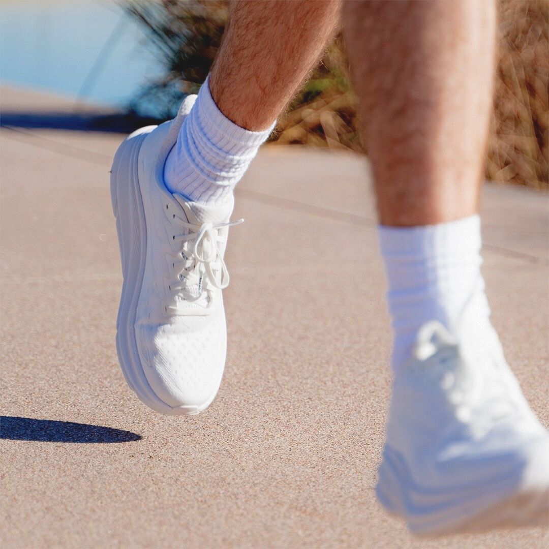 White sneakers with blue soles worn on a sandy surface