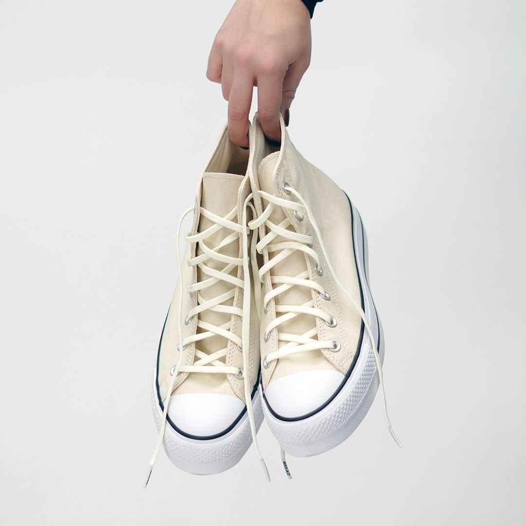 White high-top sneakers being held against a white background