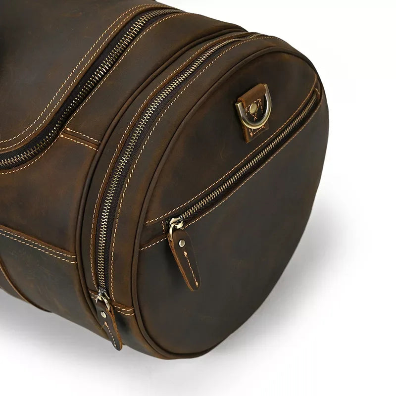 Brown leather round duffle bag side with zipper, leather pull tabs, and metal badge.