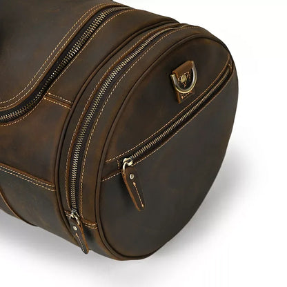 Brown leather round duffle bag side with zipper, leather pull tabs, and metal badge.