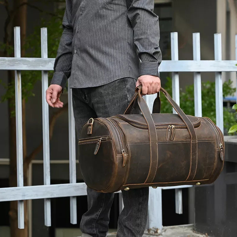 Brown leather weekender duffel bag held by top handles with front zip pockets.