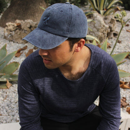 Man wearing a blue cap and sweater sitting outdoors with plants in the background