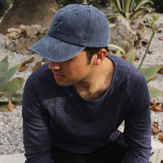 Man wearing a blue cap and sweater sitting outdoors with plants in the background
