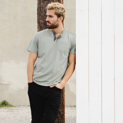 Green Striped Men's Henley T-Shirt model shot leaning against a white wall