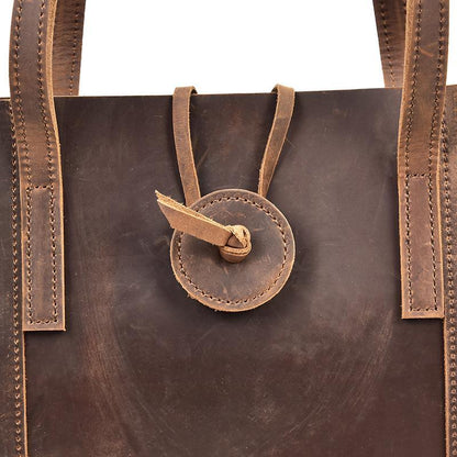Leather tote bag front close-up with oval snap clasp and vertical stitched strap panels