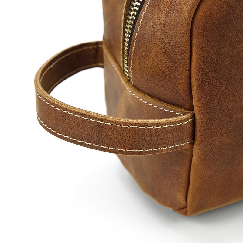 Brown leather toiletry bag corner detail with stitched strap and metal zipper pull