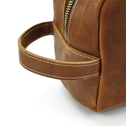 Brown leather toiletry bag corner detail with stitched strap and metal zipper pull