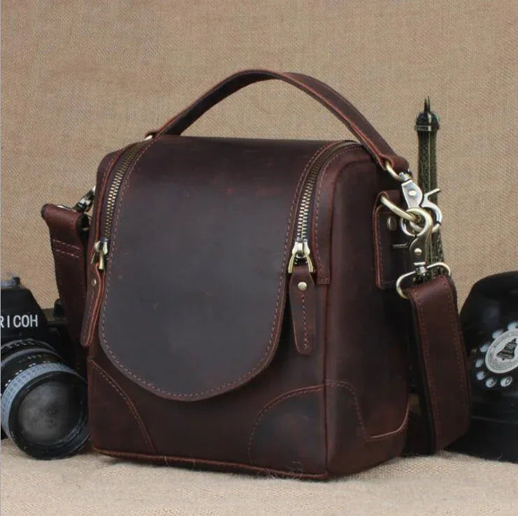 Small brown leather camera bag with front flap and brass hardware, adjustable strap