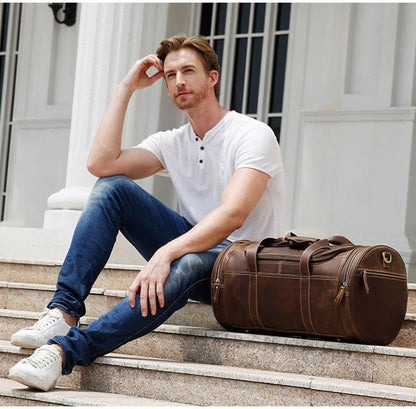 Brown leather round duffle bag with top handle and shoulder strap, brass hardware.