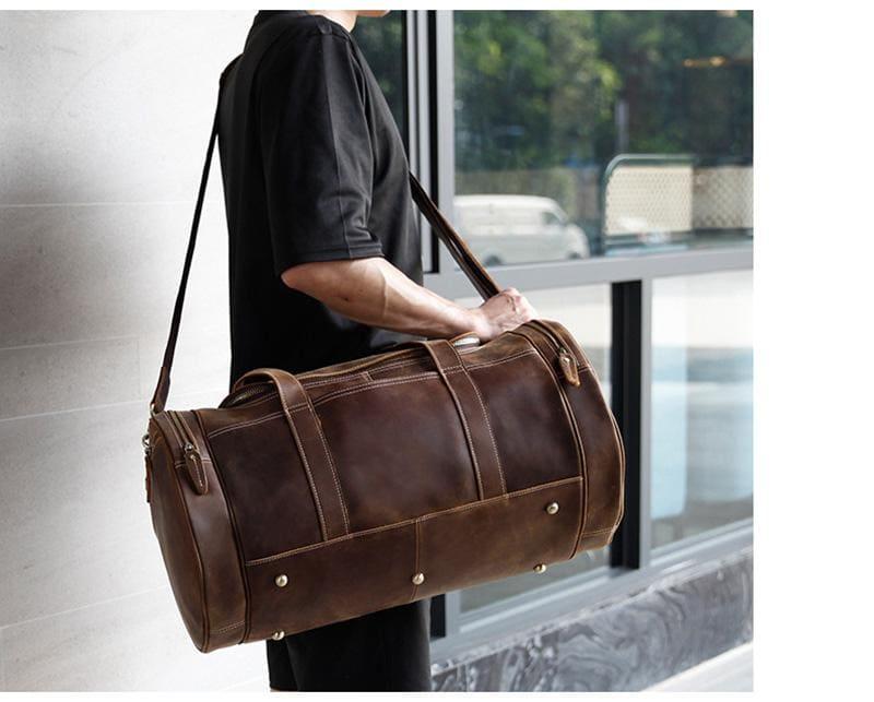 Brown leather duffel bag carried by the top handle with crossbody strap.