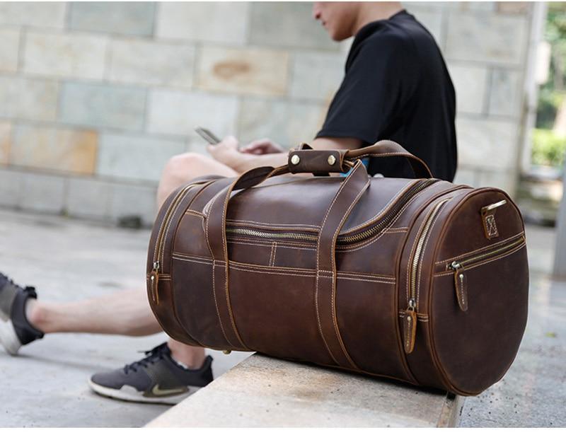 Brown leather weekender duffel bag on the floor with top handle and side zip pocket.