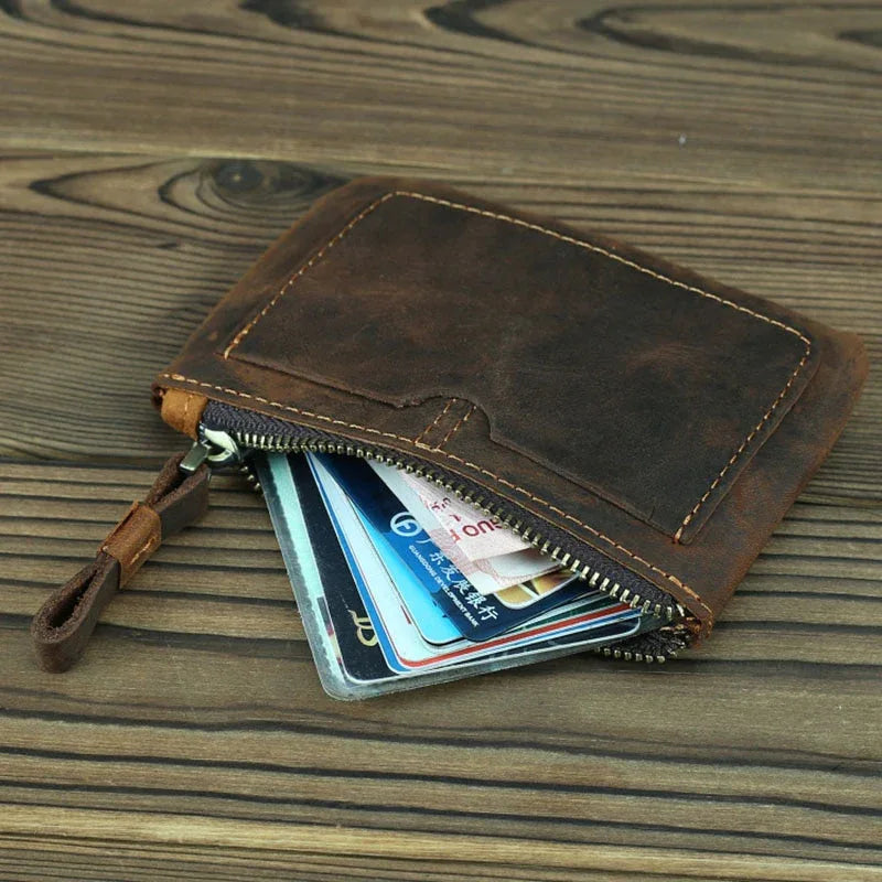 Brown leather coin purse with zipper open, showing a few cards inside.