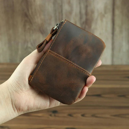 Brown leather coin purse in hand, with zipper closure and stitched edges.